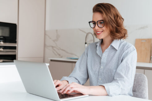 Elegant smiling woman in glasses and striped shirt using laptop